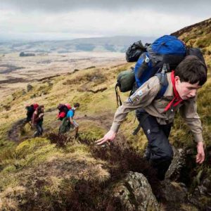 A cub scout climbing a large hill with a rucksack on his back