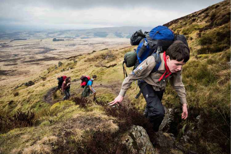 A cub scout climbing a large hill with a rucksack on his back